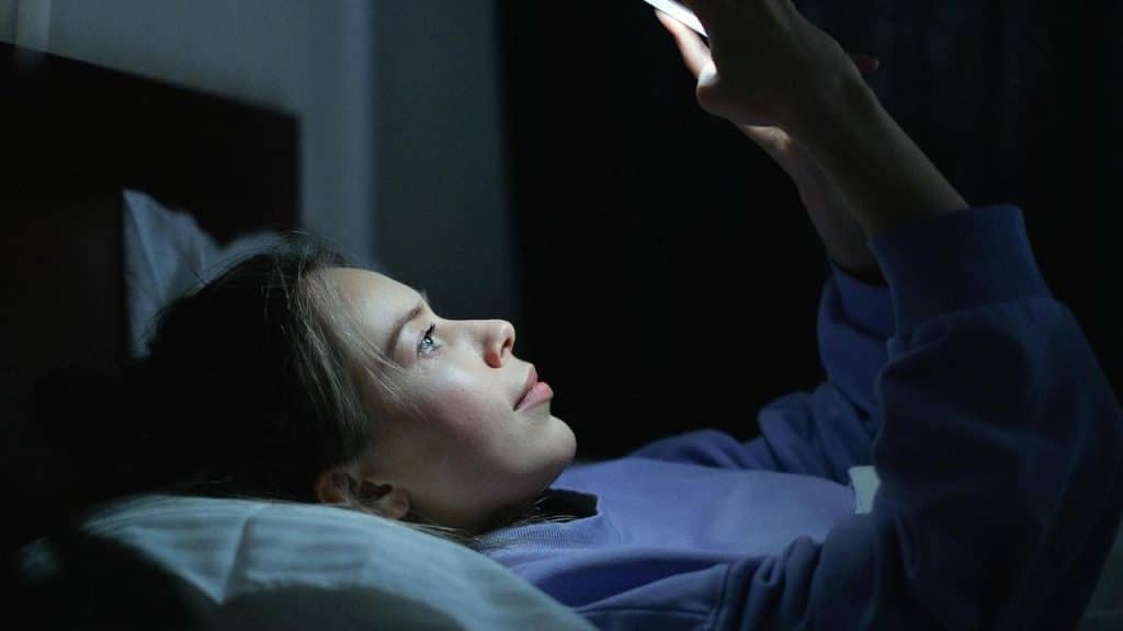 A girl lying in bed at night looking at her phone.