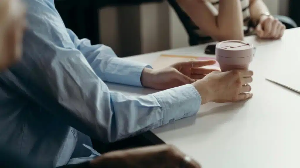 A person holding a reusable coffee cup while sitting at a table with others.
