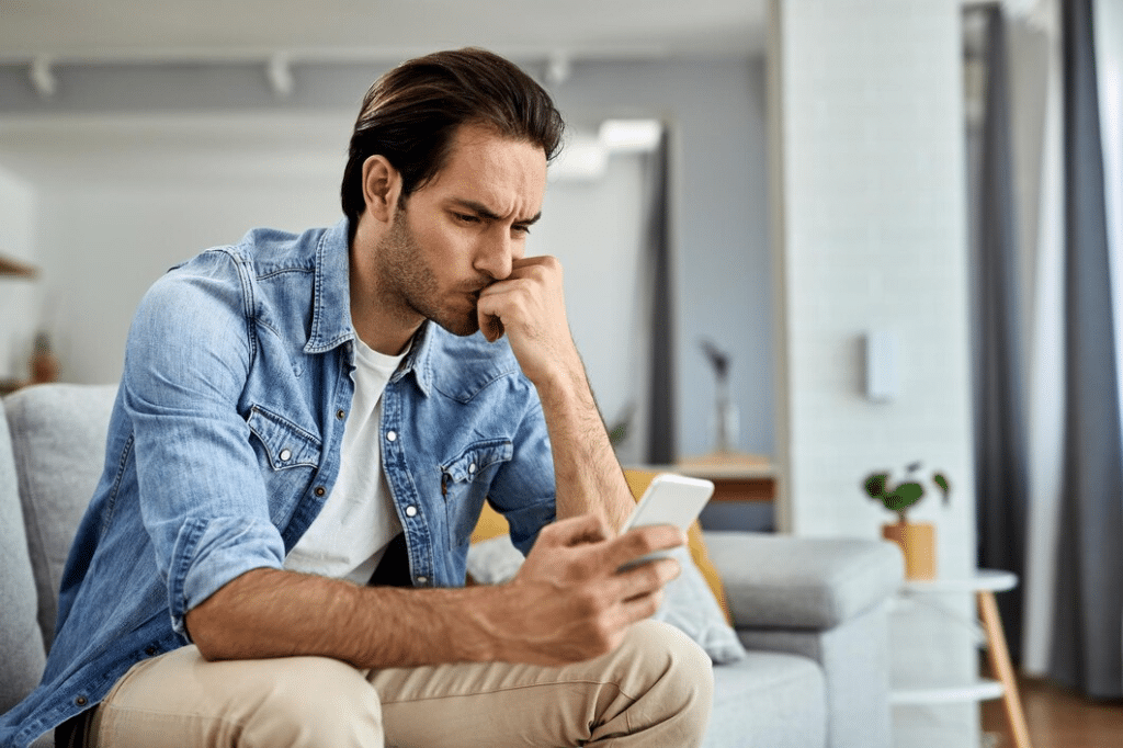 Young worried man sitting and reading text message