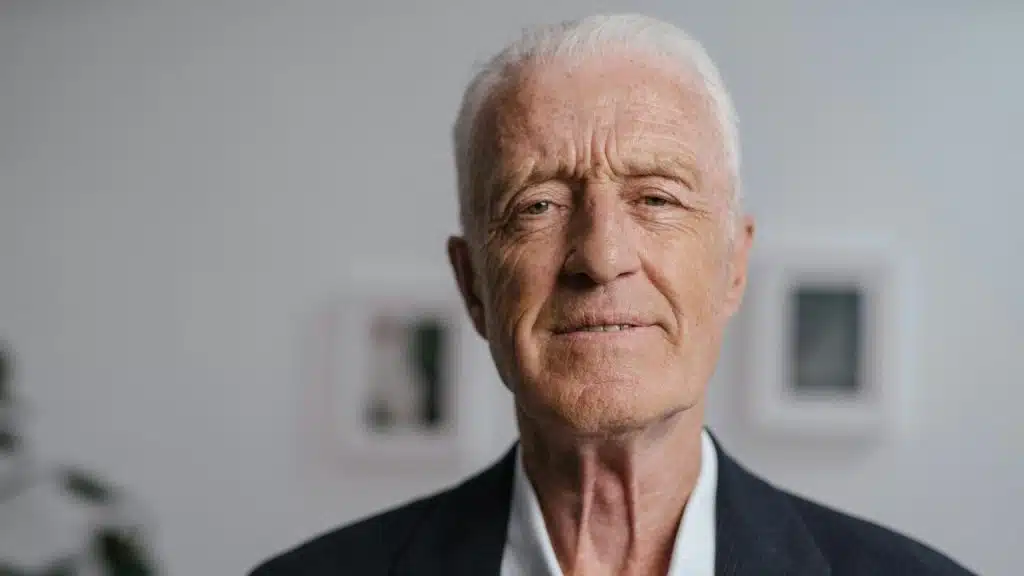A close-up portrait of an older man with white hair looking directly at the camera.