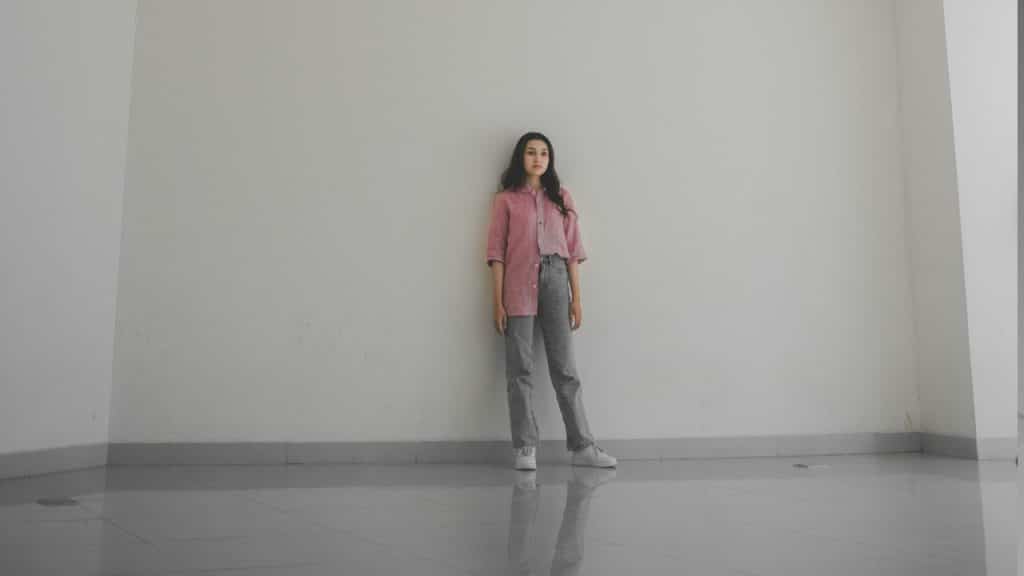 A man standing while leaning against a wall in an empty room.