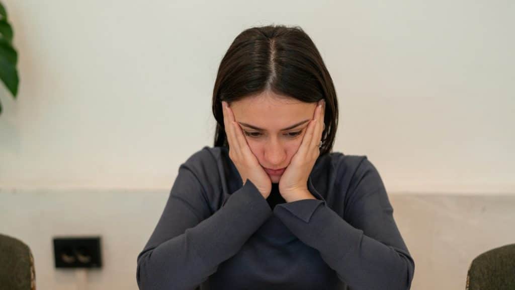 A sad woman looks down while holding her face in her hands.