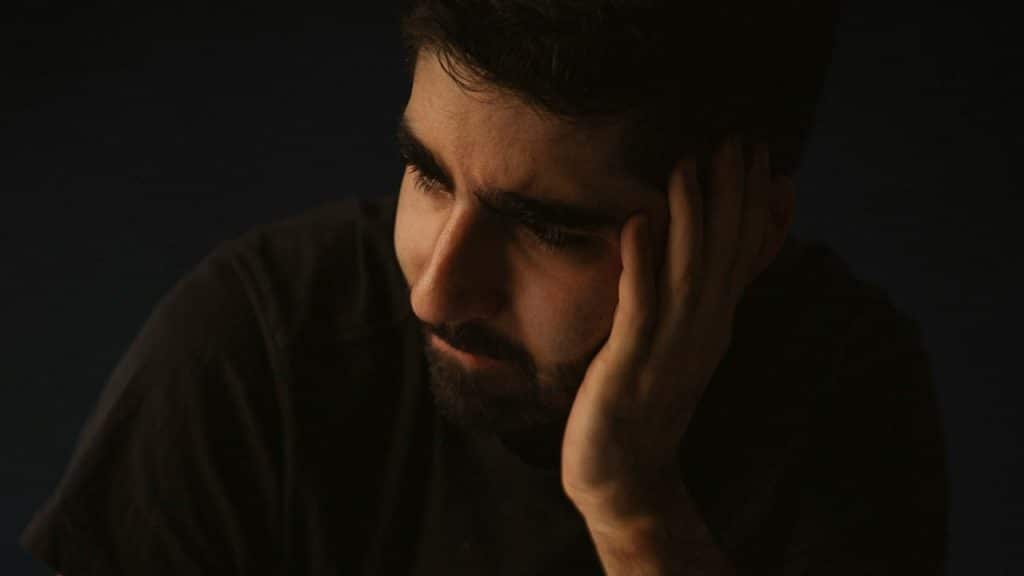 A bearded man looking upset and holding his hand up to his face.