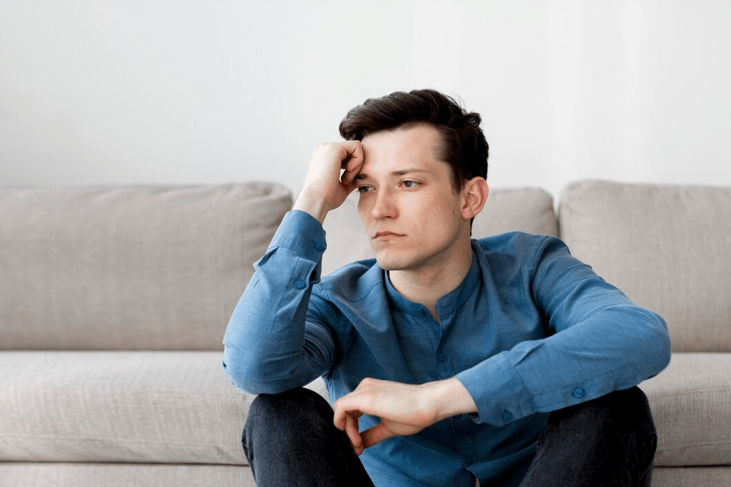 Man upset sitting down in front of sofa