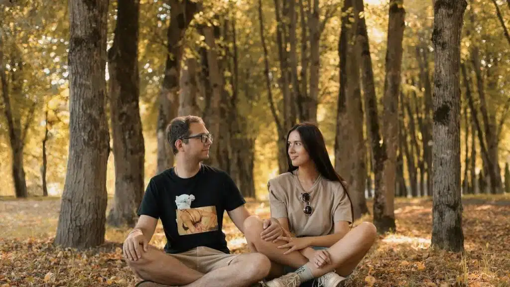 A man and a woman sitting on the ground in a forest.