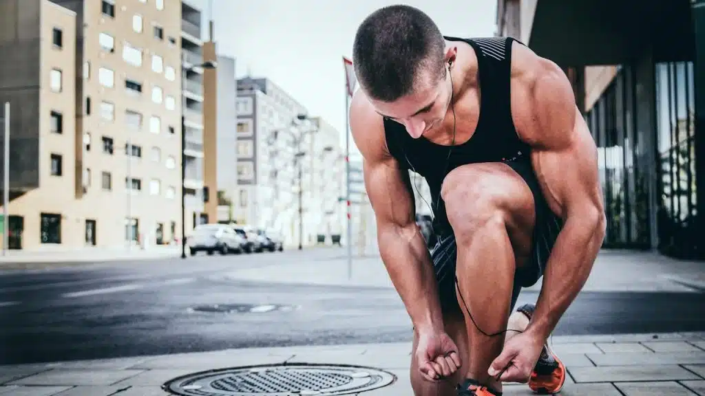 A muscular man tying his shoelaces while getting ready for a run on the streets.