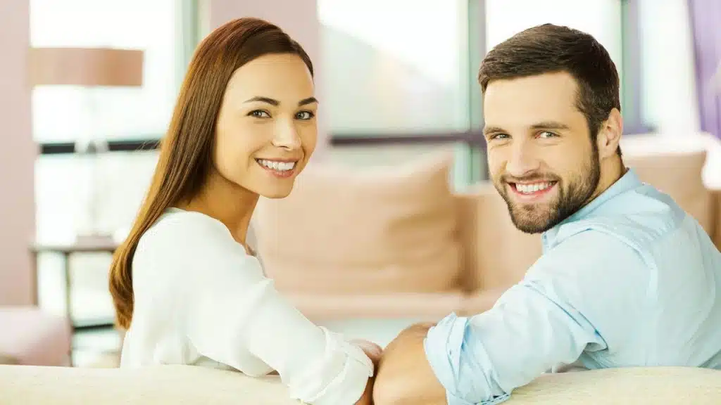 Rear view of a beautiful, young, loving couple sitting together on the couch and smiling.