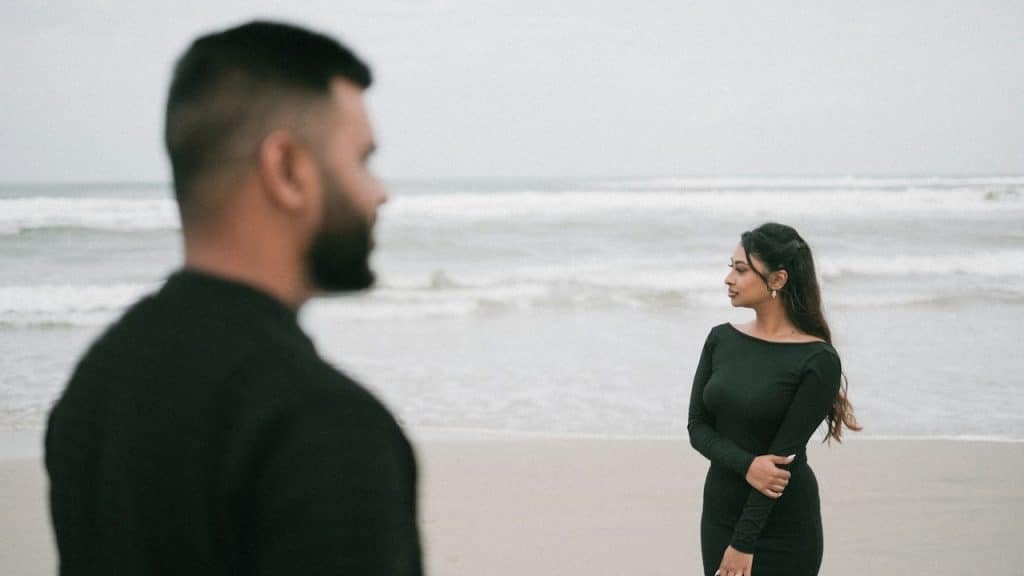 A couple on the beach is facing the ocean.