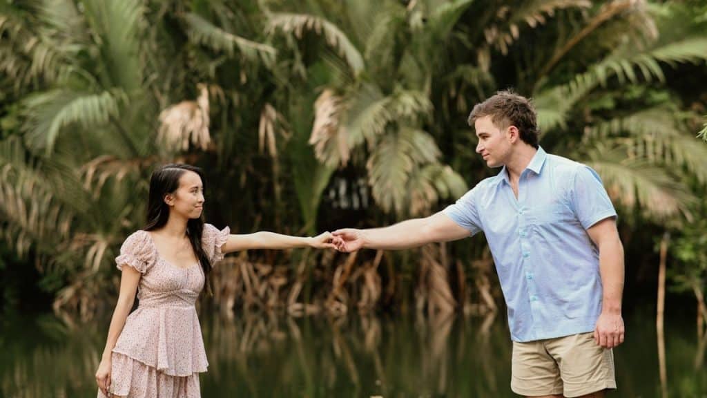 A couple holding hands by a reflective body of water.