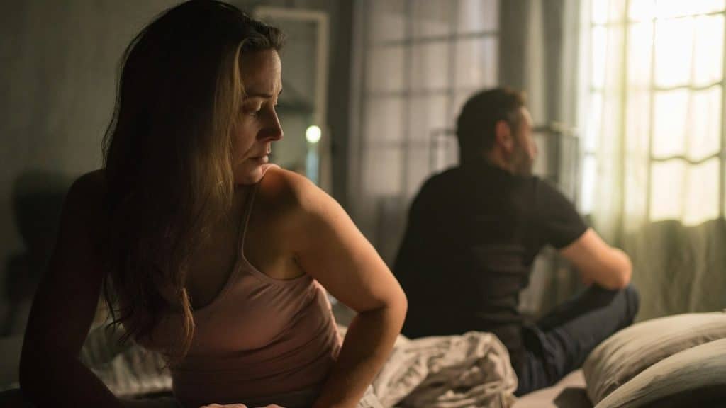 An unhappy couple sitting on the bed after a fight.