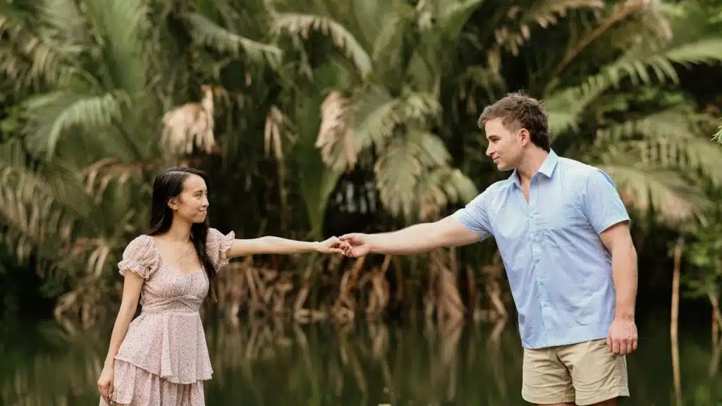 A couple holding hands by a reflective body of water.