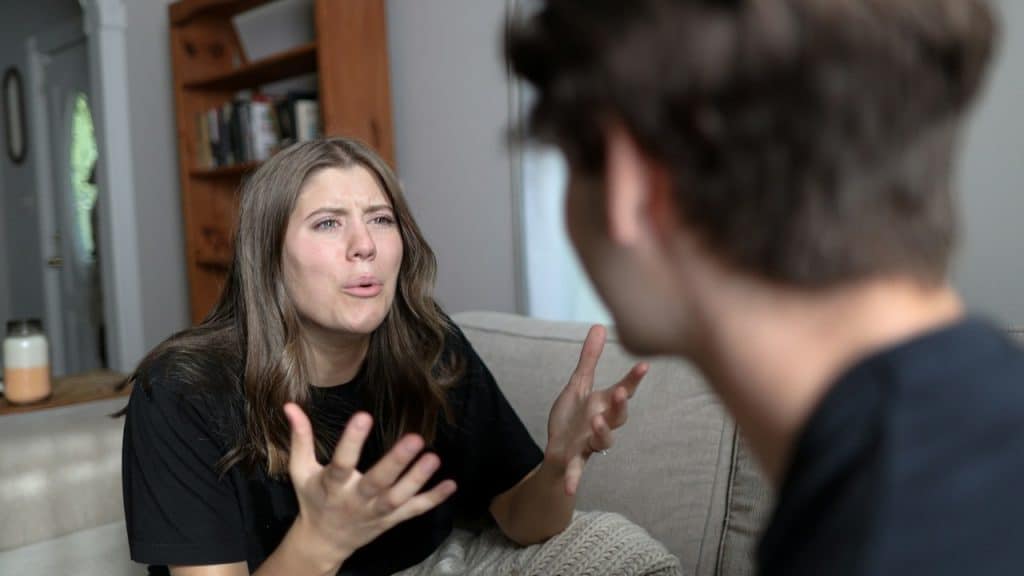A woman arguing with her husband while sitting on a sofa next to him.
