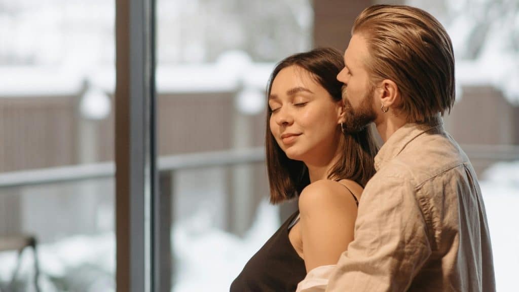 A man with a beard standing behind a woman, leaning his face close to her head.