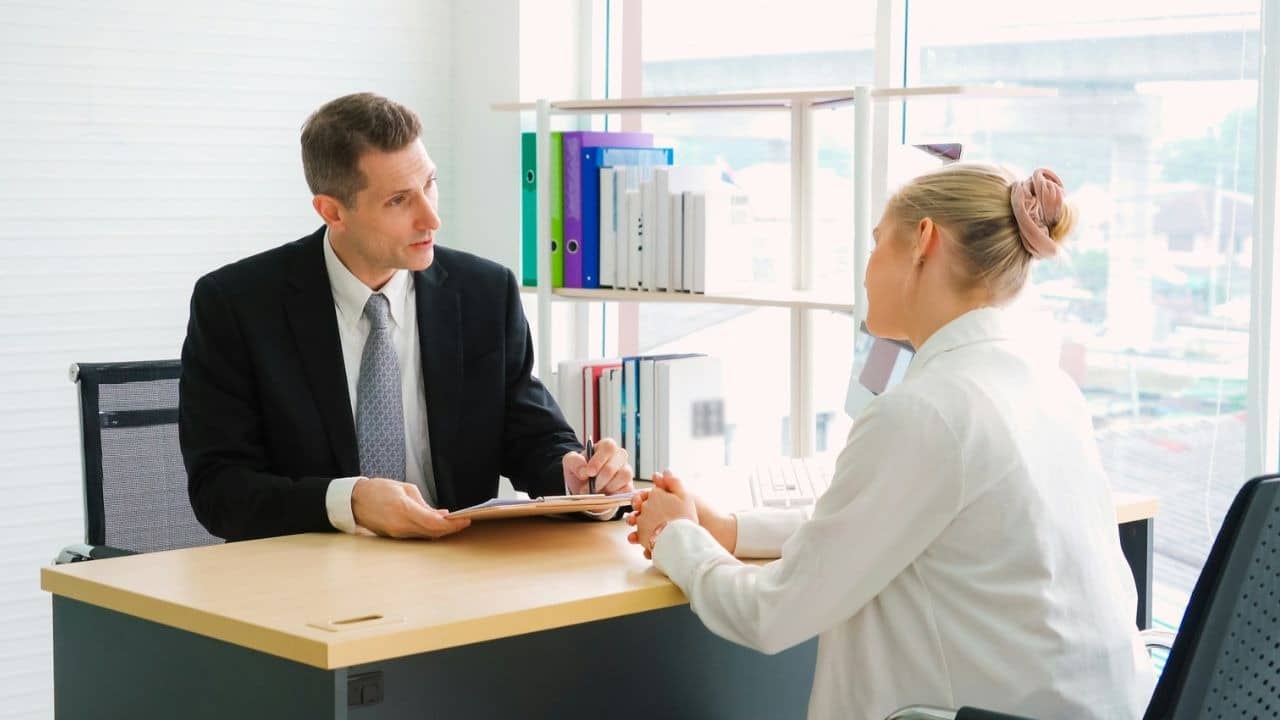 A man in a suit and a woman in white sit across from each other.