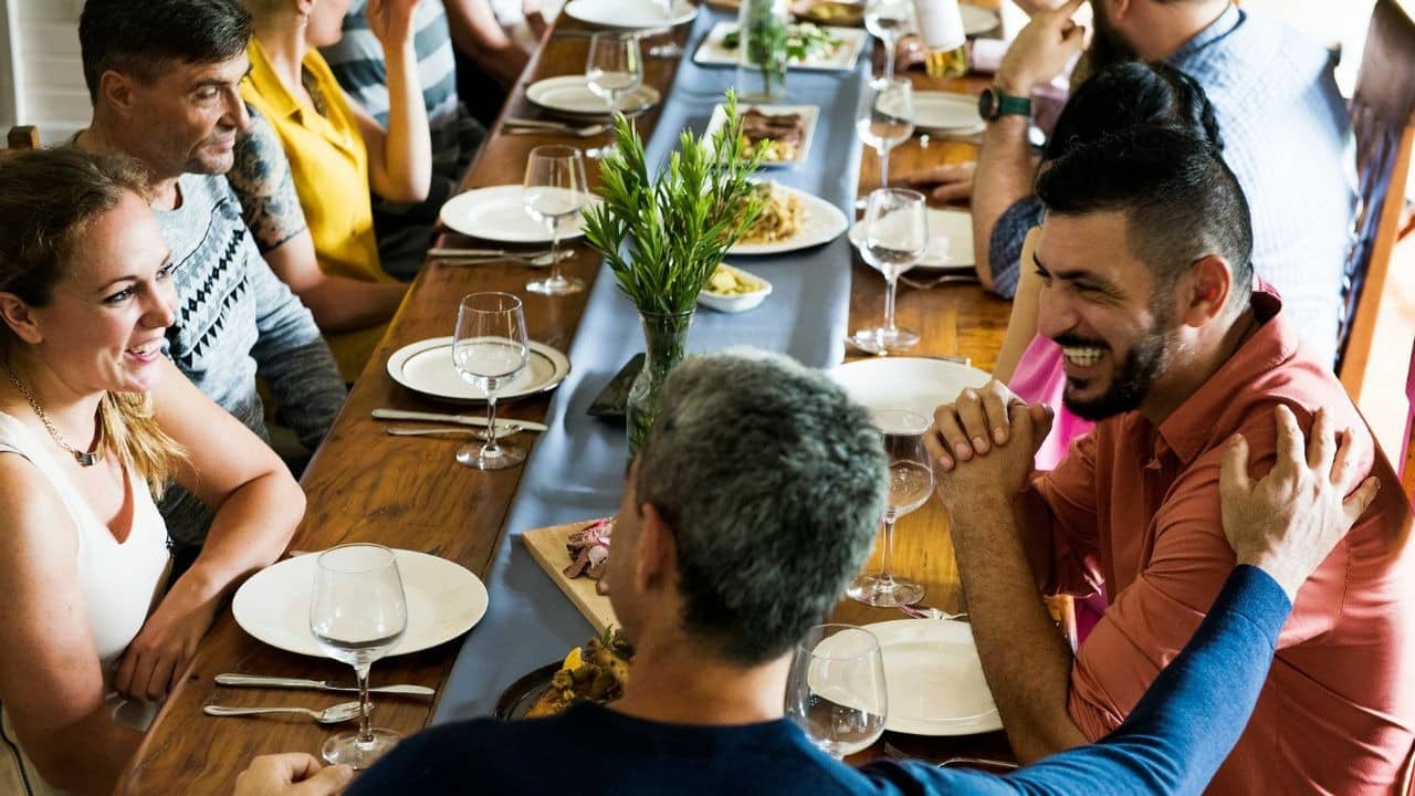 A large group of people sit around a long wooden table eating and talking together.