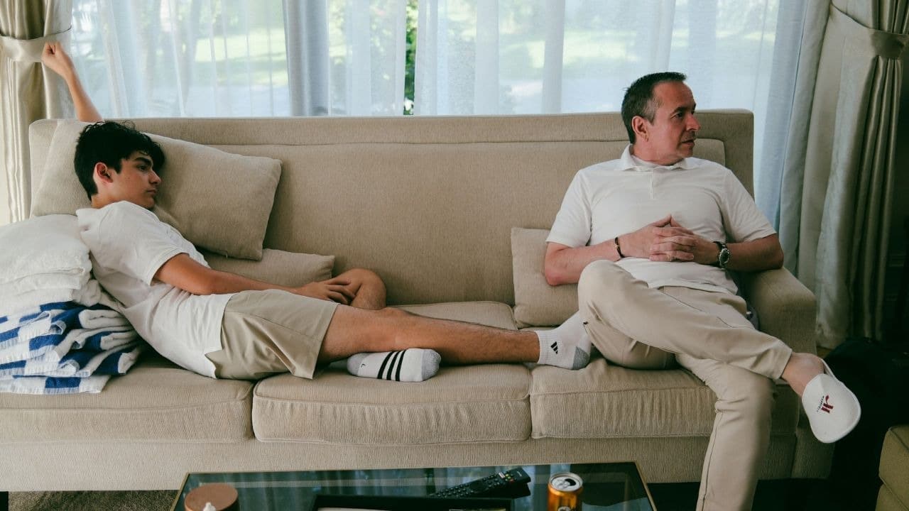 A man and a teenage boy sit on opposite ends of a sofa looking away from each other.