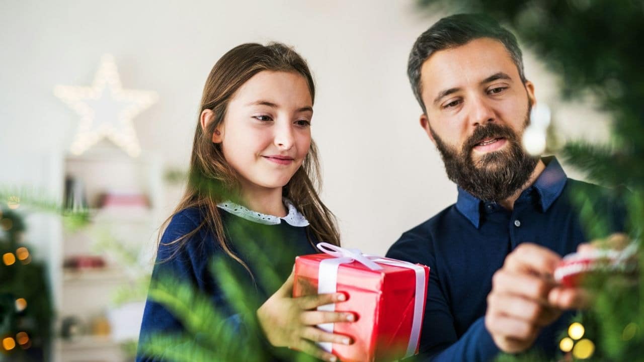 A bearded man and a young girl stand together while holding a red gift box.