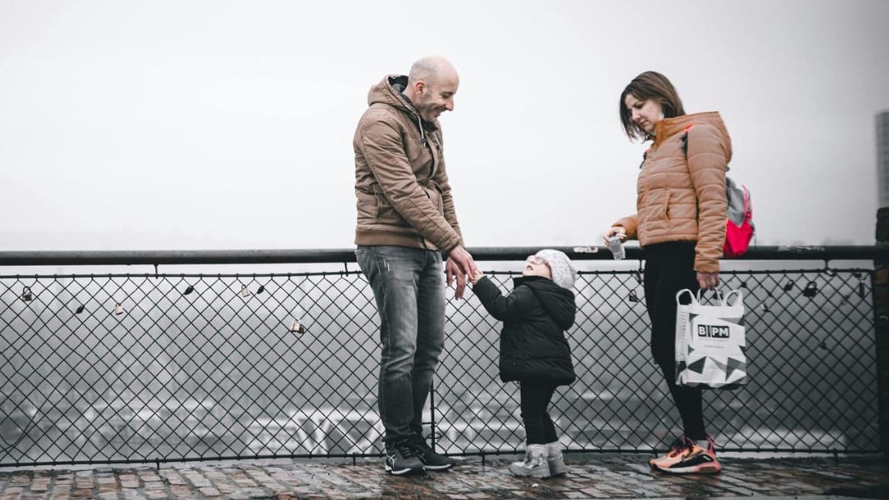A man, woman, and small child stand on a bridge outdoors on a cloudy day.