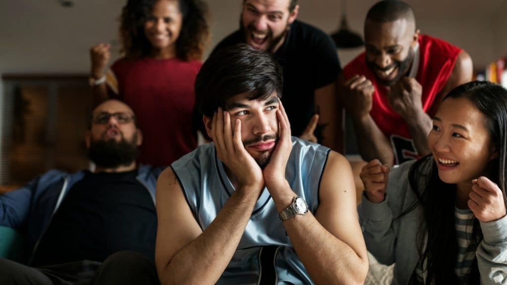 A man sits with his face in his hands while people around him cheer and gesture.