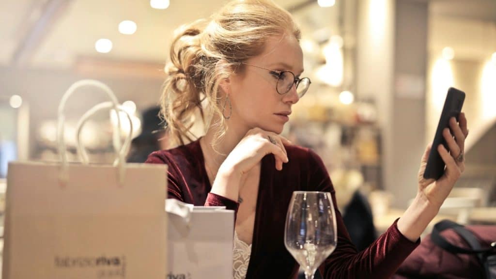 A woman with glasses and a red velvet dress looks at her phone at a table.