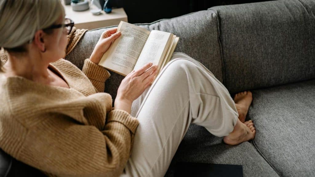 A woman relaxes on a couch reading a book.