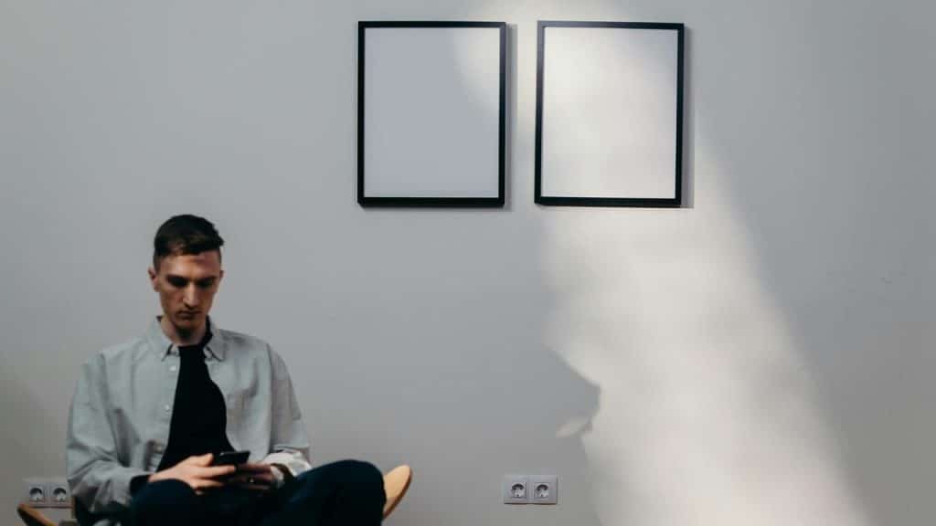 A man sitting in a minimalist room using a smartphone