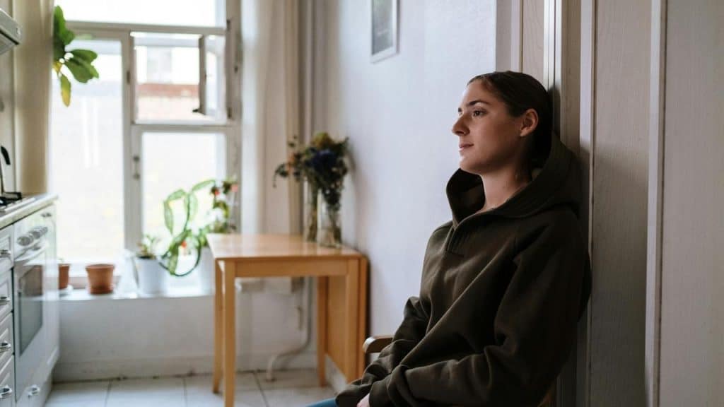 A woman in a hoodie sitting indoors, leaning against a wall 