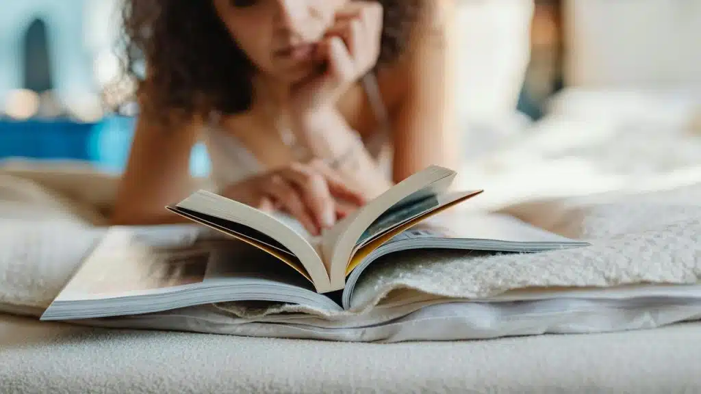 A person lying on a bed reading an open book.