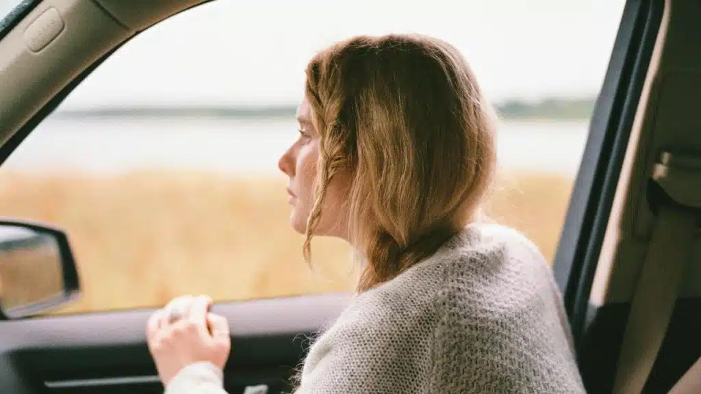 A woman sitting in a car looking out the window at a field.