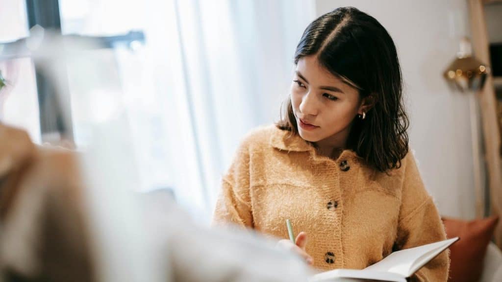 A woman in a tan sweater writing in a notebook indoors.