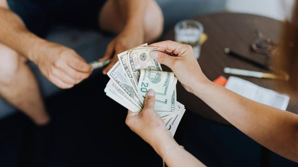 A person counting U.S. dollar bills while another person hands over cash.
