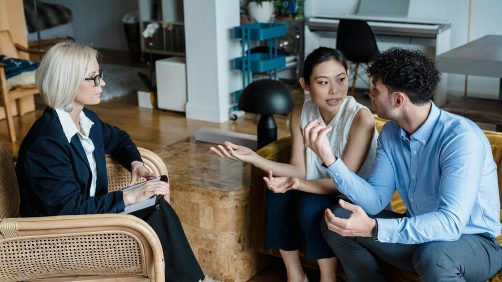 A couple talking with a woman taking notes during a counseling session.