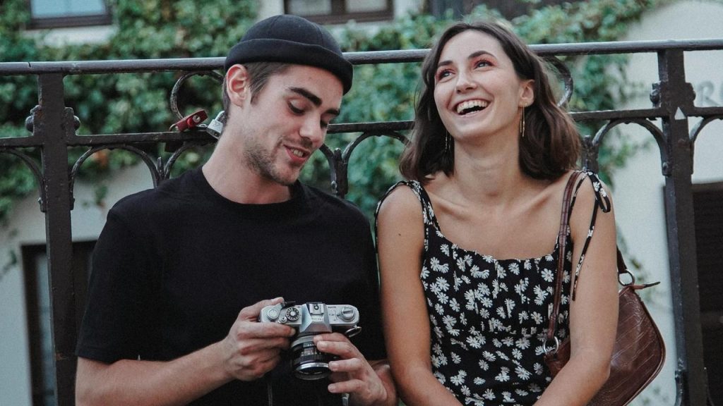A couple laughing together while one holds a camera outdoors.