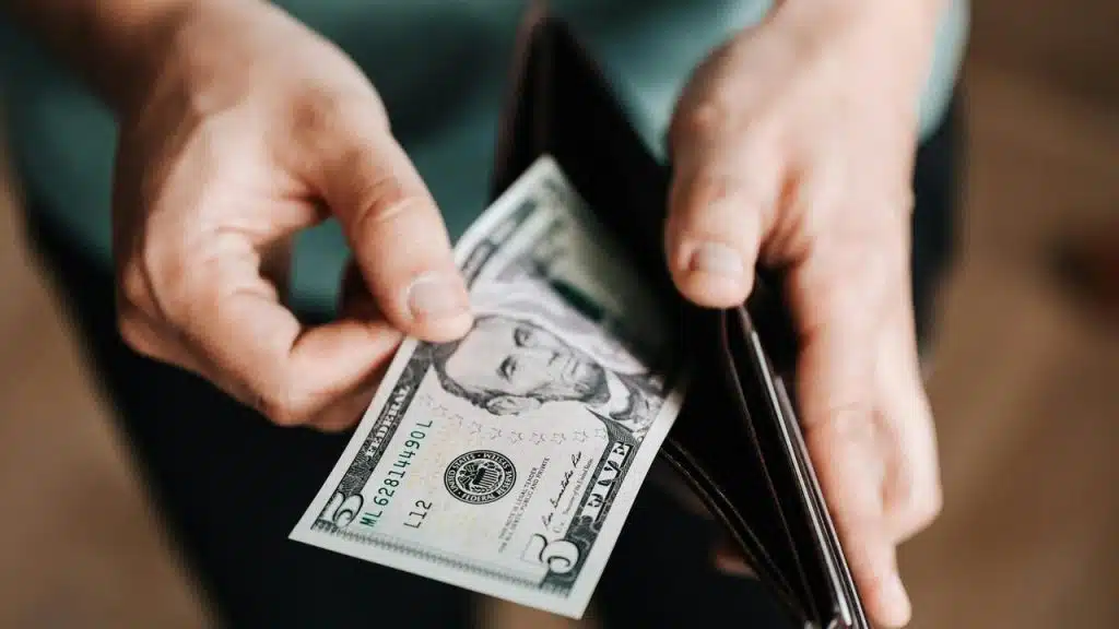 A hand pulling a five-dollar bill from a wallet.