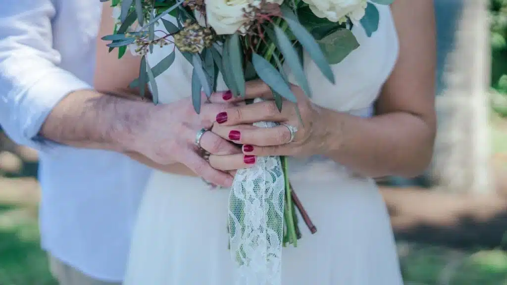 A couple holding a bouquet together with wedding rings visible.