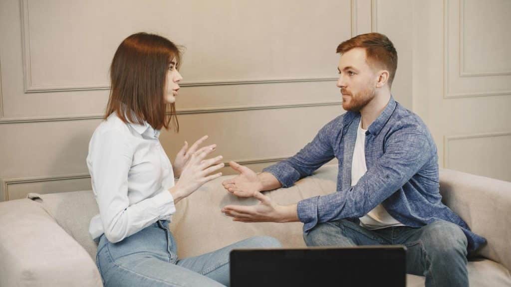 A man and woman sitting on a couch having a serious discussion.