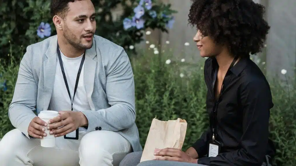 A man and woman talking outdoors while holding coffee and a snack bag.