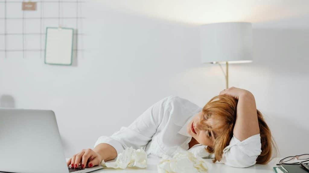 A tired woman resting her head on her arm while using a laptop at a desk.