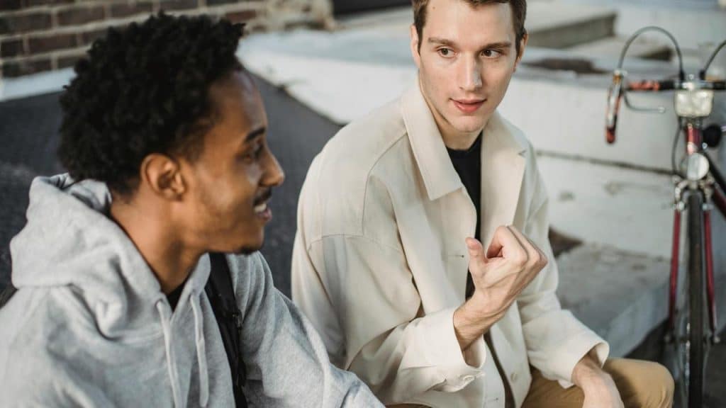A pair of men sitting outdoors and talking near a bicycle.