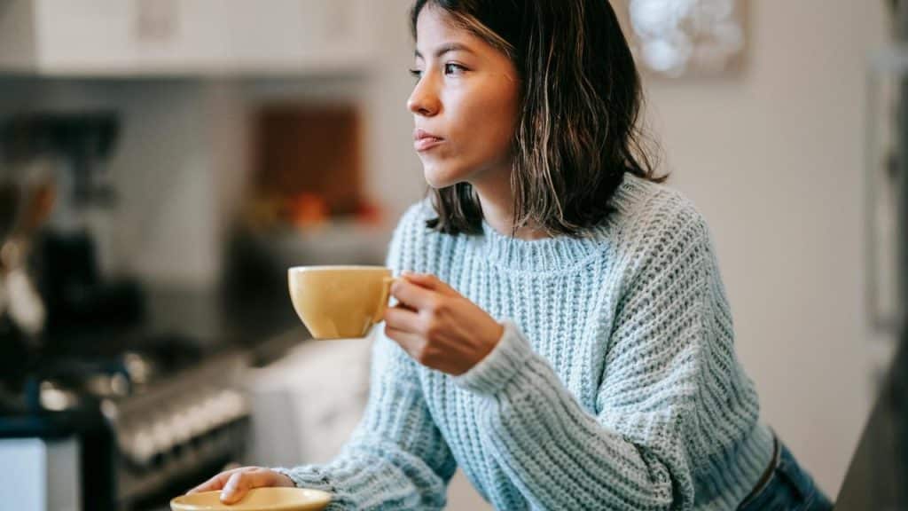 A woman holding a cup of coffee while standing in a kitchen.