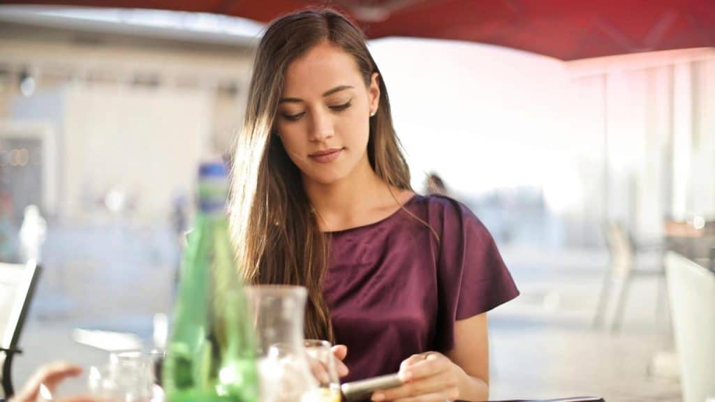 A woman sitting at an outdoor café table while looking at her phone.
