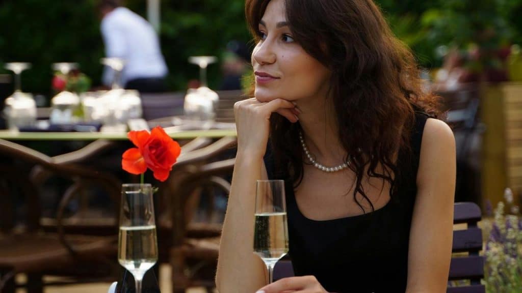 A woman sitting at an outdoor restaurant table with a glass of champagne and a red rose.
