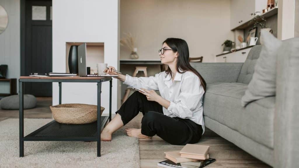A woman sitting on the floor working on a laptop at a coffee table in a living room.