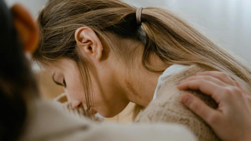 A woman with her head down being comforted by someone’s hand on her shoulder.