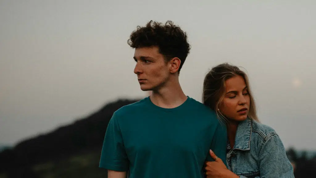 A young couple in nature holding hands but looking away from each other.