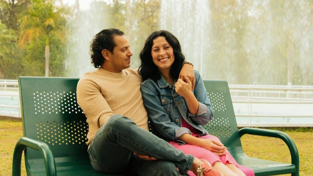 A couple sits on a bench in front of a fountain.