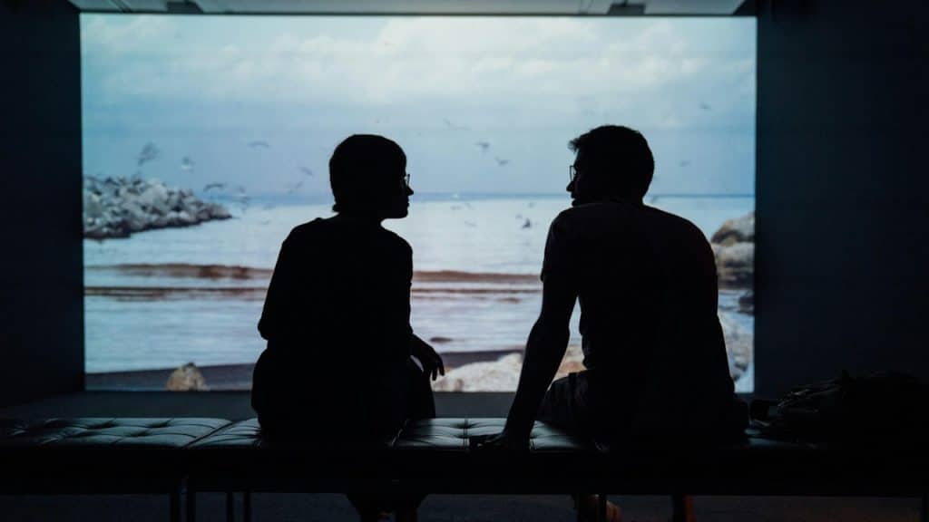 A silhouette of a man and a woman sitting on an ottoman.