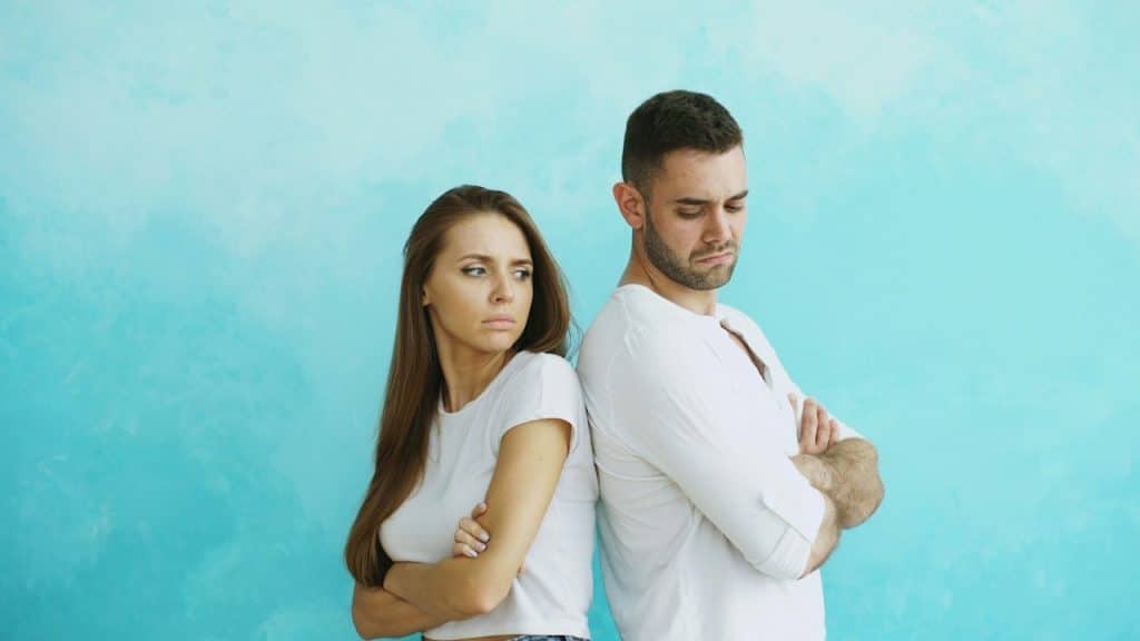 A couple standing back-to-back with arms crossed.