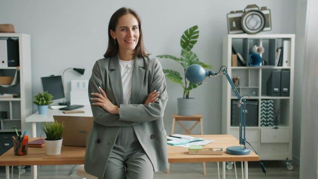 A woman wearing a gray suit standing in an office with her arms crossed.