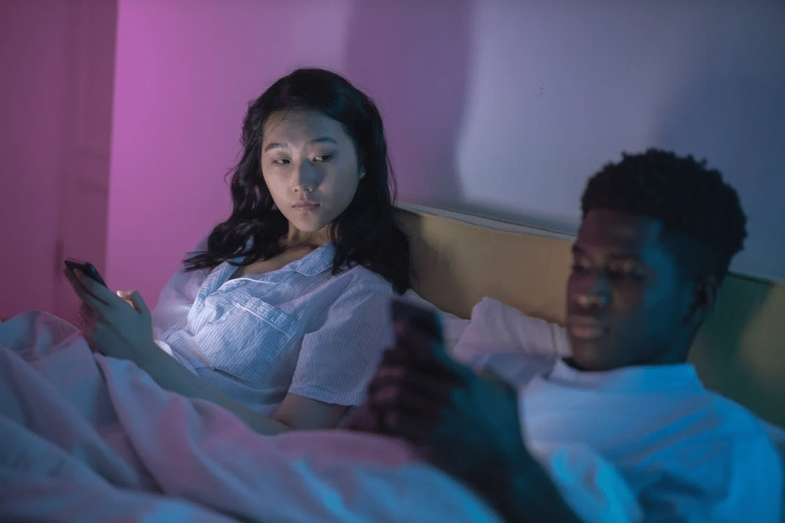 Couple in bed on phones ignoring each other